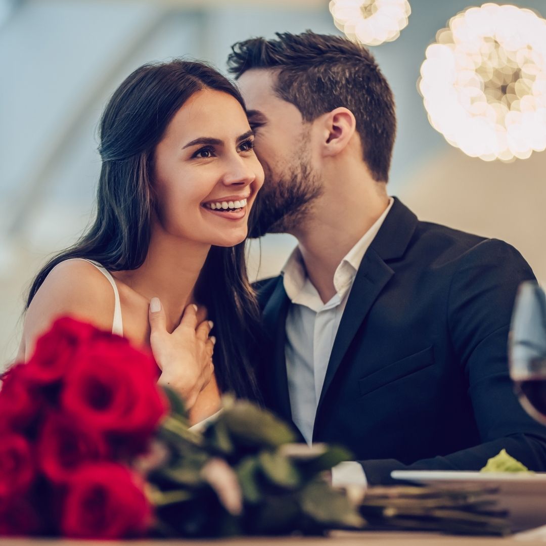 a man whispering into a woman's ear at a romantic dinner